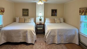 Une chambre avec deux lits simples, un ventilateur de plafond, une table de chevet avec une lampe et un tapis.