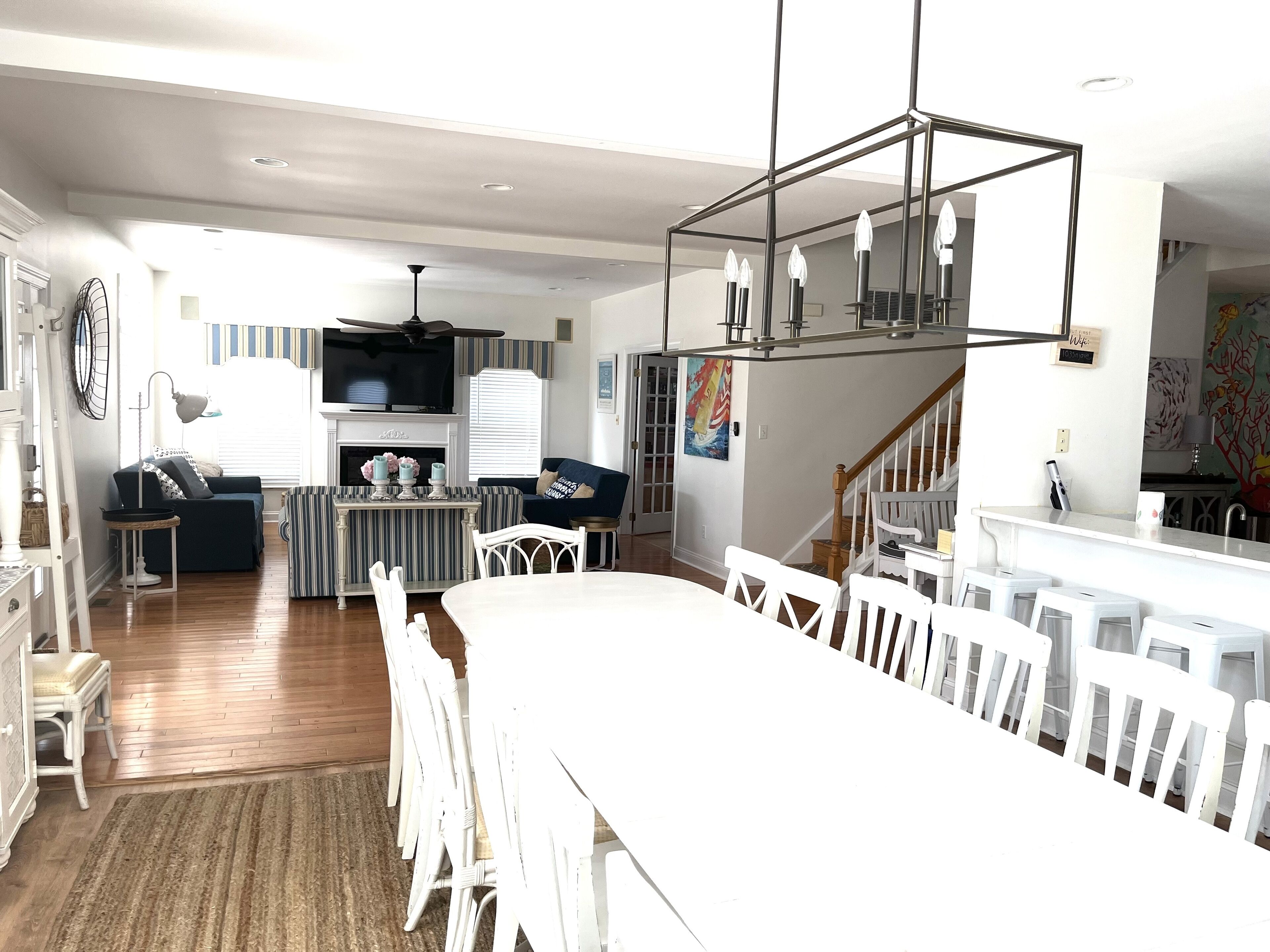 A spacious living area with a large white dining table, a fireplace, a television, and a staircase leading to an upper level.