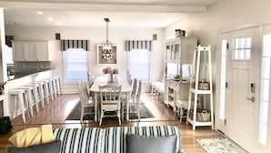 Una cocina moderna con armarios blancos, un comedor con cortinas a rayas y una sala de estar con un sofá a rayas.