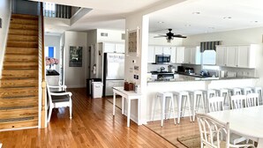 Una cocina moderna con armarios blancos, una isla central con taburetes de bar y una escalera de madera.