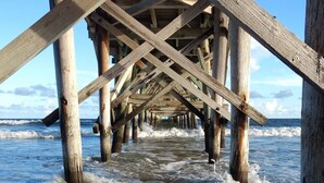 Un muelle de madera que se adentra en el océano, con olas rompiendo a su alrededor.
