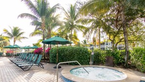 Un espace piscine doté de chaises longues et d’un jacuzzi, le tout entouré de palmiers et de verdure.