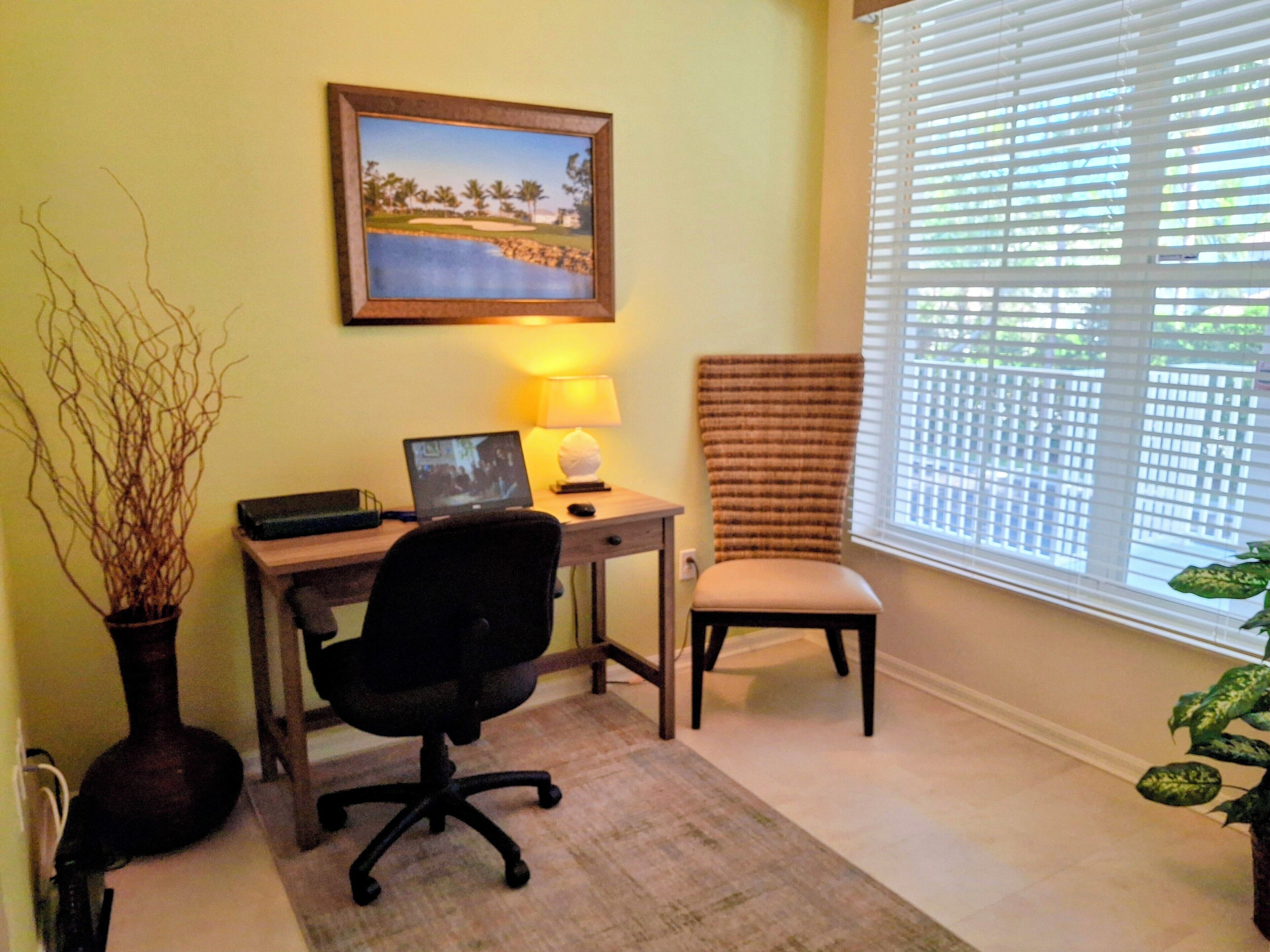 A home office with a desk, chair, computer, lamp, and a framed picture on the wall.