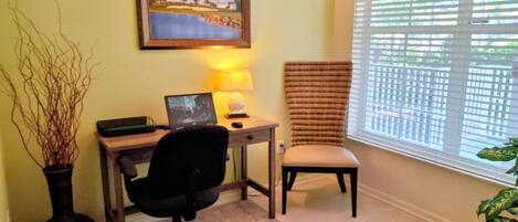 A home office with a desk, chair, computer, lamp, and a framed picture on the wall.