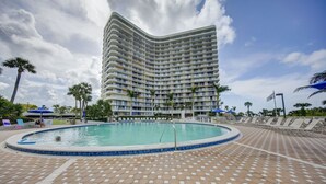 Un hotel grande con piscina rodeada de sillones de descanso y palmeras.