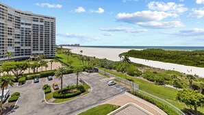 Un hotel con estacionamiento, vistas a la playa y un edificio grande al fondo.
