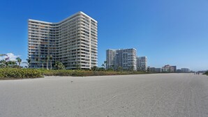 Un hotel frente a la playa con fachada curva, varios balcones y una playa arenosa al frente.