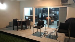 Une terrasse avec une table à manger et des chaises, une petite table et un barbecue.