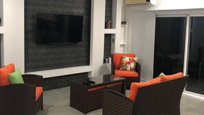 Un salon moderne doté d’un téléviseur à écran plat, de meubles en osier et d’un ventilateur de plafond.