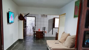 Een kamer met een bed, een eettafel met stoelen, een televisie en een betegelde vloer.