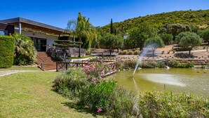 A modern building with a pool, surrounded by lush greenery and a hill in the background. - Stunning 3 bedroom en-suite house in farm with pool (Estoi)