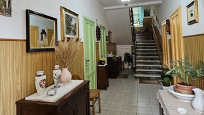 Un couloir aux murs lambrissés, un escalier et divers objets décoratifs, notamment des vases et des plantes.