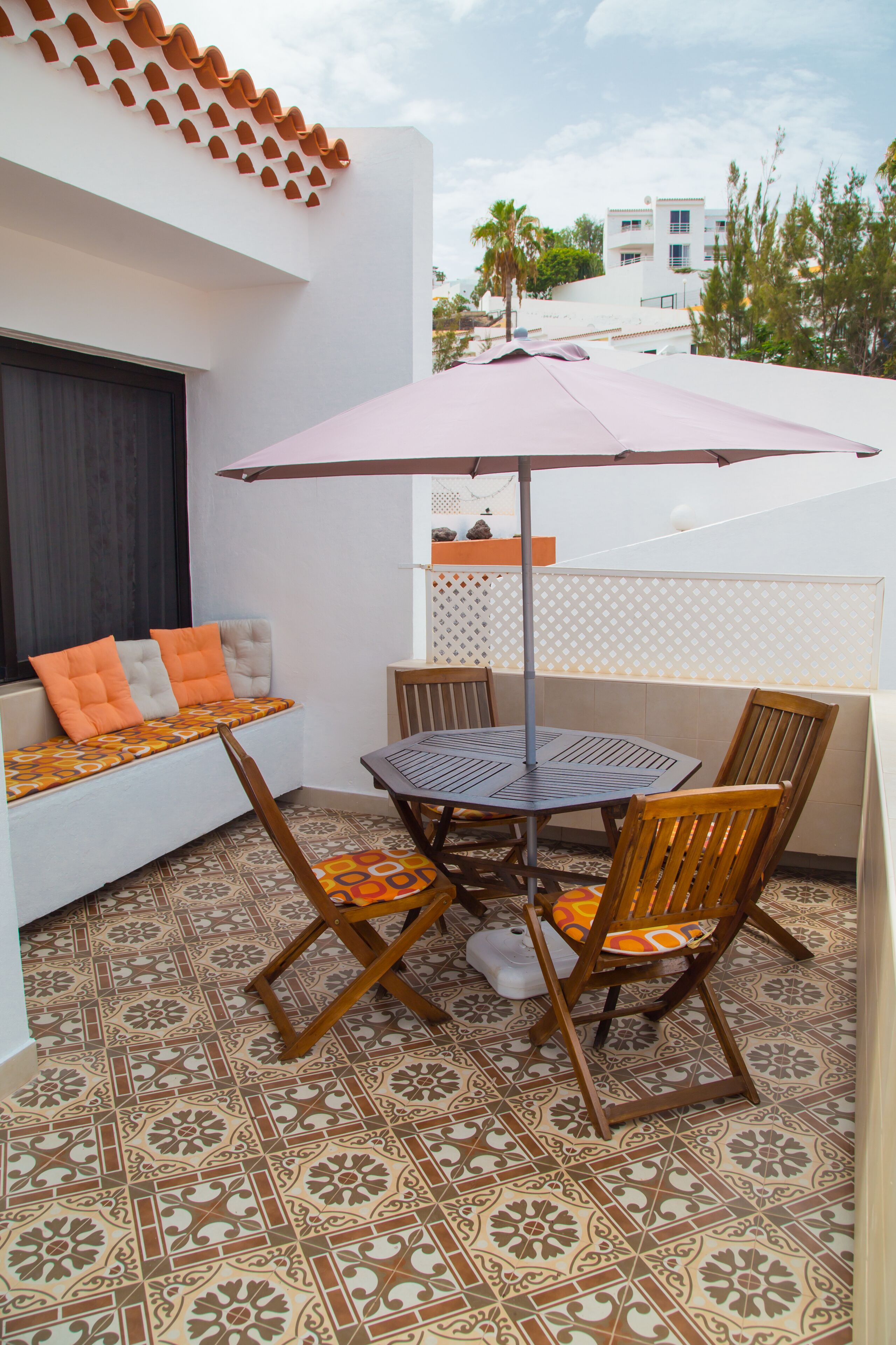Eine Terrasse mit Tisch und Stühlen, einer gepolsterten Bank und einer Zierwand.