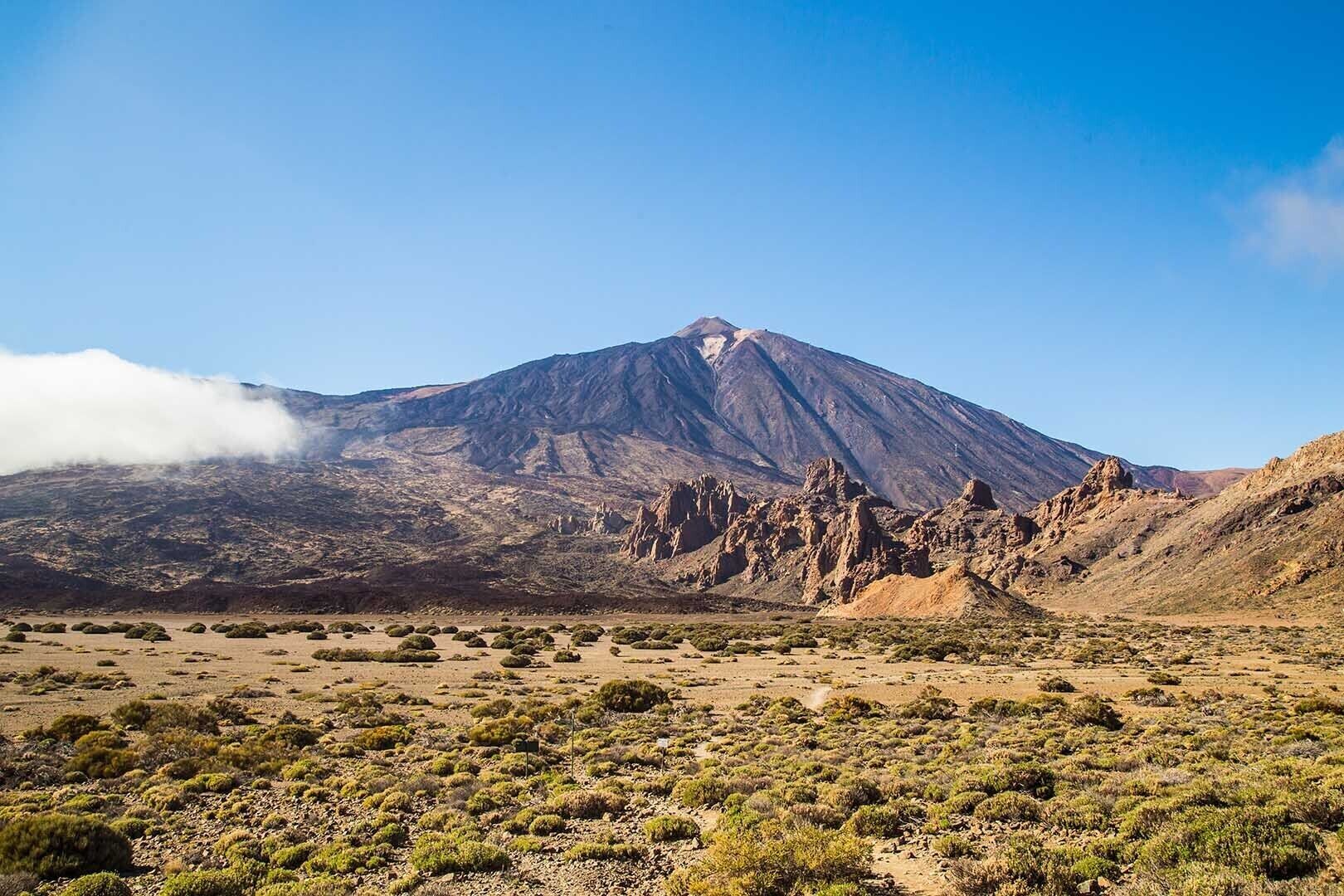 A mountainous landscape with a prominent peak, sparse vegetation, and a clear sky.