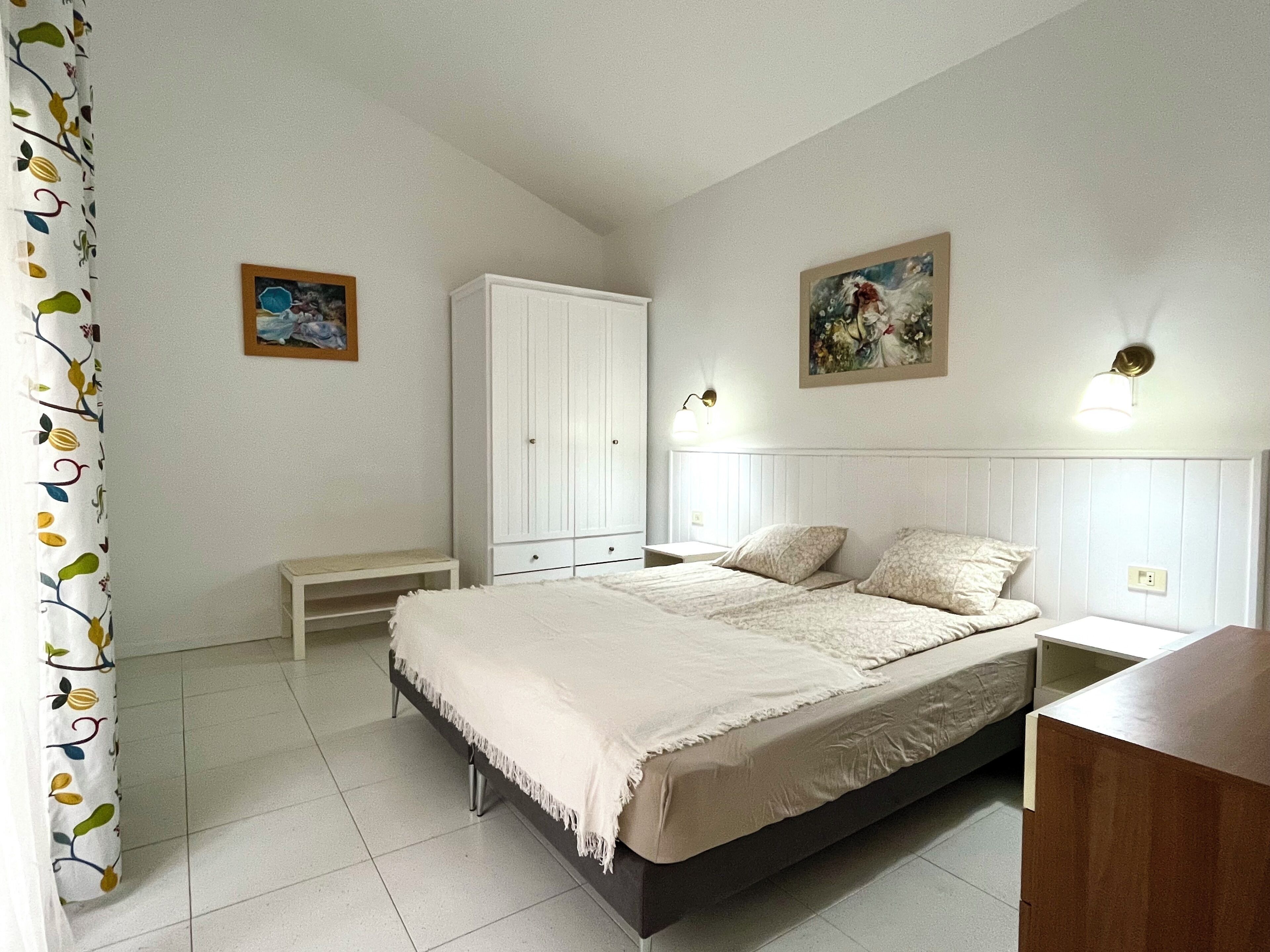Ein Schlafzimmer mit Bett, Kleiderschrank, einer Bank und zwei Wandleuchten.
