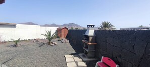 A backyard with a barbecue grill, a red bench, and a view of mountains.
