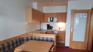 Cocina compacta con armarios de madera, microondas y lavavajillas. Hay un banco con cojines junto a la mesa de comedor.
