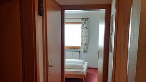 Un estrecho pasillo con puertas de madera a ambos lados que dan a un dormitorio con cama y ventana con cortinas.