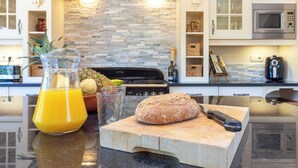 Eine Küche mit Steinrückwand, einem Brot auf einem Schneidebrett, einem Glas Orangensaft und einer Ananas.