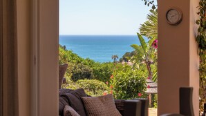 Blick von einem Zimmer mit großem Fenster auf einen Garten und das Meer.