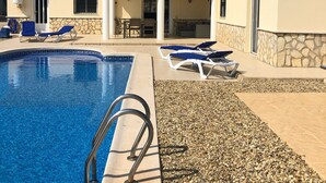 Piscina com espreguiçadeiras, um muro de pedra e um telhado telhado.