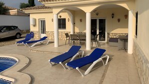 Uma área externa coberta com cadeiras de descanso, piscina e espaço para refeições.