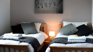A hotel room with two beds, each with a pillow, a bedside table with a lamp, and a wall-mounted artwork of footprints. - Beautiful detatched cottage situated within a small hamlet near Bamburgh. (waren mill)
