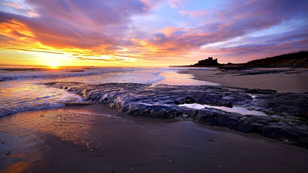 A beach with waves, a sunset, and rocky terrain. - Beautiful detatched cottage situated within a small hamlet near Bamburgh. (waren mill)