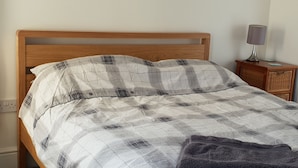 A neatly made bed with a plaid bedspread and two pillows, a bedside lamp, and a wicker nightstand with a lamp. - Lovely Light, Spacious Flat With Sea View (Herne Bay)