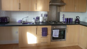 A modern kitchen with wooden cabinets, a stainless steel range hood, a built-in oven, and a sink with a purple towel hanging on the door. - Lovely Light, Spacious Flat With Sea View (Herne Bay)