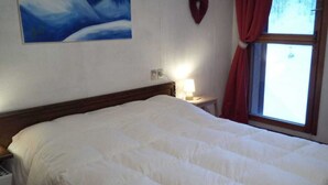 Een hotelkamer met een groot bed, een nachtkastje, een lamp, een schilderij aan de muur en een raam met gordijnen.