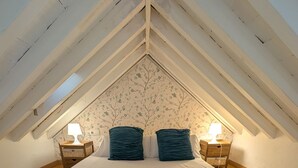 A bedroom with a sloped ceiling, a bed with white linens, two dark pillows, and two bedside lamps.