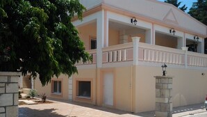 A two-story building with a balcony, a stone pillar, and a small garden area. - father's house in kissamos (Korfalonas)