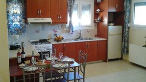 A compact kitchen with wooden cabinets, a white stove, and a dining table set for four. - father's house in kissamos (Korfalonas)