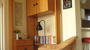 Ein Zimmer mit einem Korbstuhl, Holzschränken, einem Schreibtisch mit Büchern und einem Wandbild mit abstrakter Kunst.