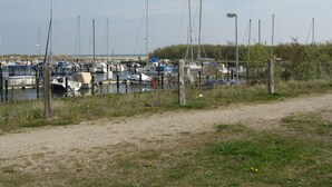 Ein Yachthafen mit mehreren angestaubten Booten, umgeben von grünen Wiesen und einem Feldweg.