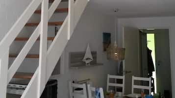 Een eetruimte met een witte tafel en stoelen, een kleine decoratie van een zeilboot, en een trap naar een hoger niveau.