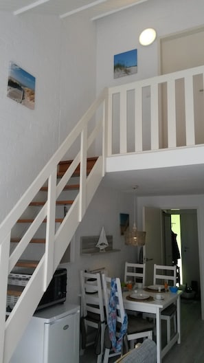 Ein Essbereich mit einem weißen Tisch und Stühlen, einer kleinen Segelboot-Dekoration und einer Treppe, die zu einer oberen Ebene führt.