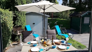 Une terrasse extérieure avec une table dressée pour le repas, entourée de chaises et d’un parasol.