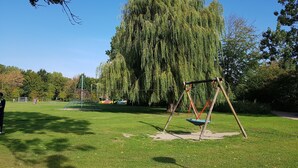 Un parc équipé d’une balançoire, d’une structure d’escalade et d’un grand saule pleureur.