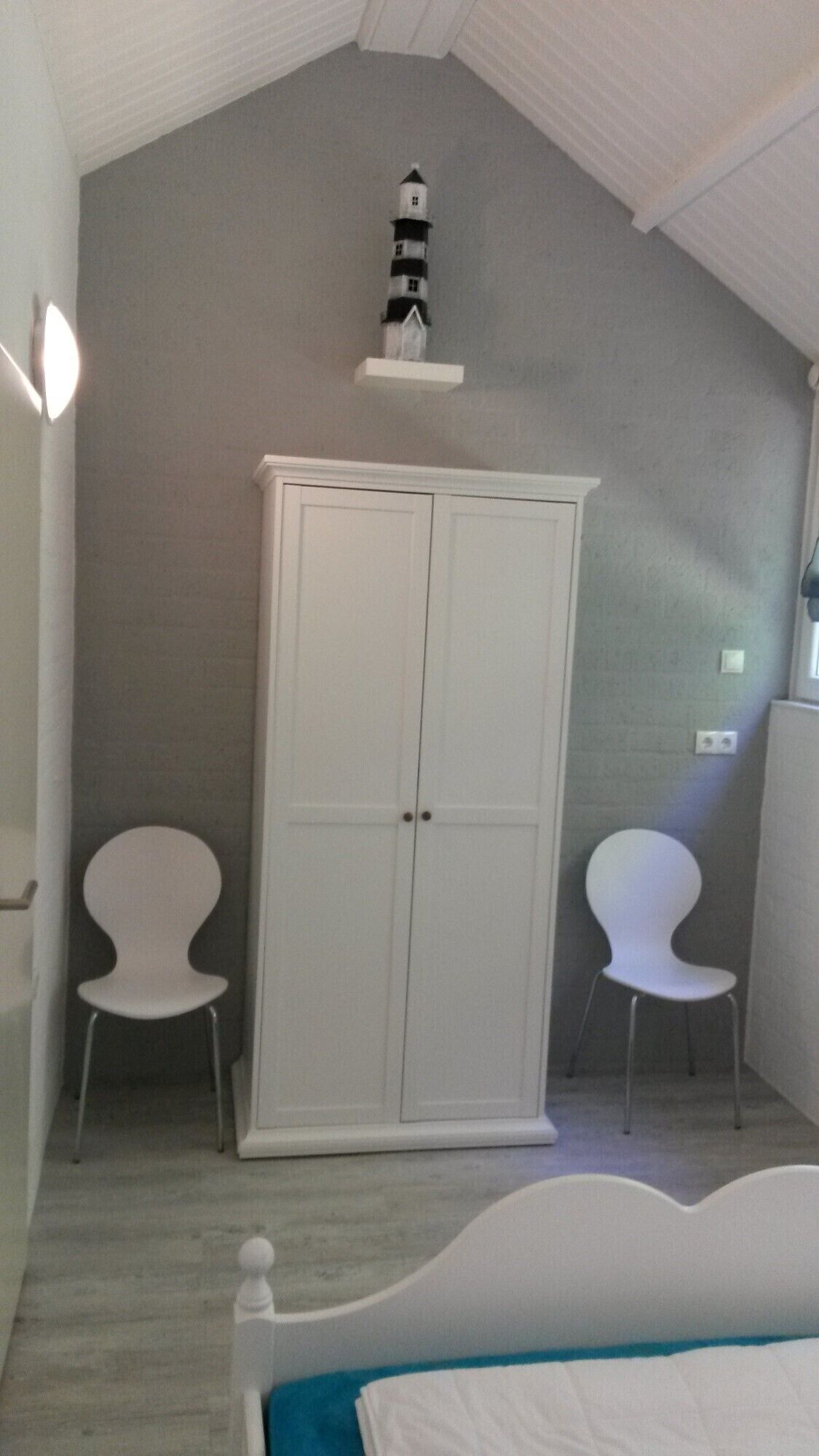 Una camera da letto con un letto, un armadio, due sedie e una piccola decorazione a forma di faro sul muro.