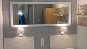 Une chambre avec deux lits, un grand miroir et une petite étagère sur laquelle est posé un modèle de bateau.