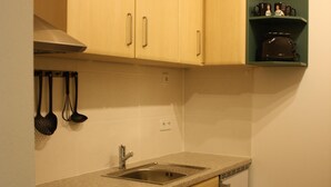 A compact kitchen with wooden cabinets, a built-in oven, a dishwasher, and a countertop with a sink. - Cozy little apartment (Südwest)