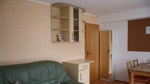 A compact living space with a green sofa, a wooden dining table, a cabinet, and a wooden door. - Cozy little apartment (Südwest)