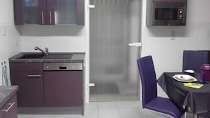 A compact kitchen with a sink, dishwasher, and a microwave. There is a door leading to another room and a table with chairs.