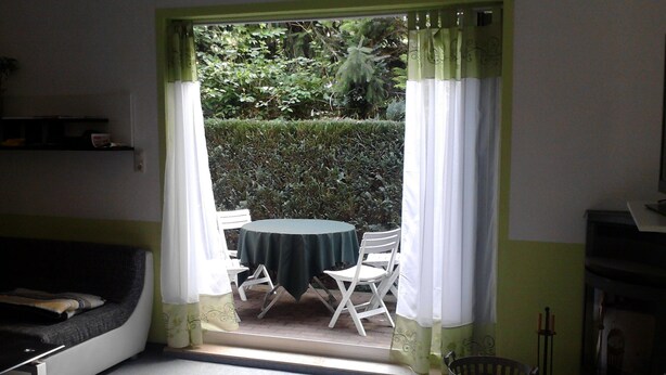 A room with a table and chairs, a sofa, a small shelf, and a window with curtains.