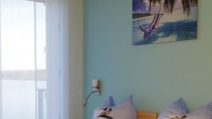 Un dormitorio con cama, almohadas, una mesita de noche, una lámpara y un cuadro con una playa.
