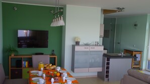 Una sala de estar moderna con comedor, paredes verdes, un televisor de pantalla plana y una cocina con una isla central.