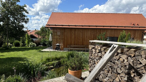 Een houten terras met een rustieke vuurkuil, een stapel hout en een potplant.
