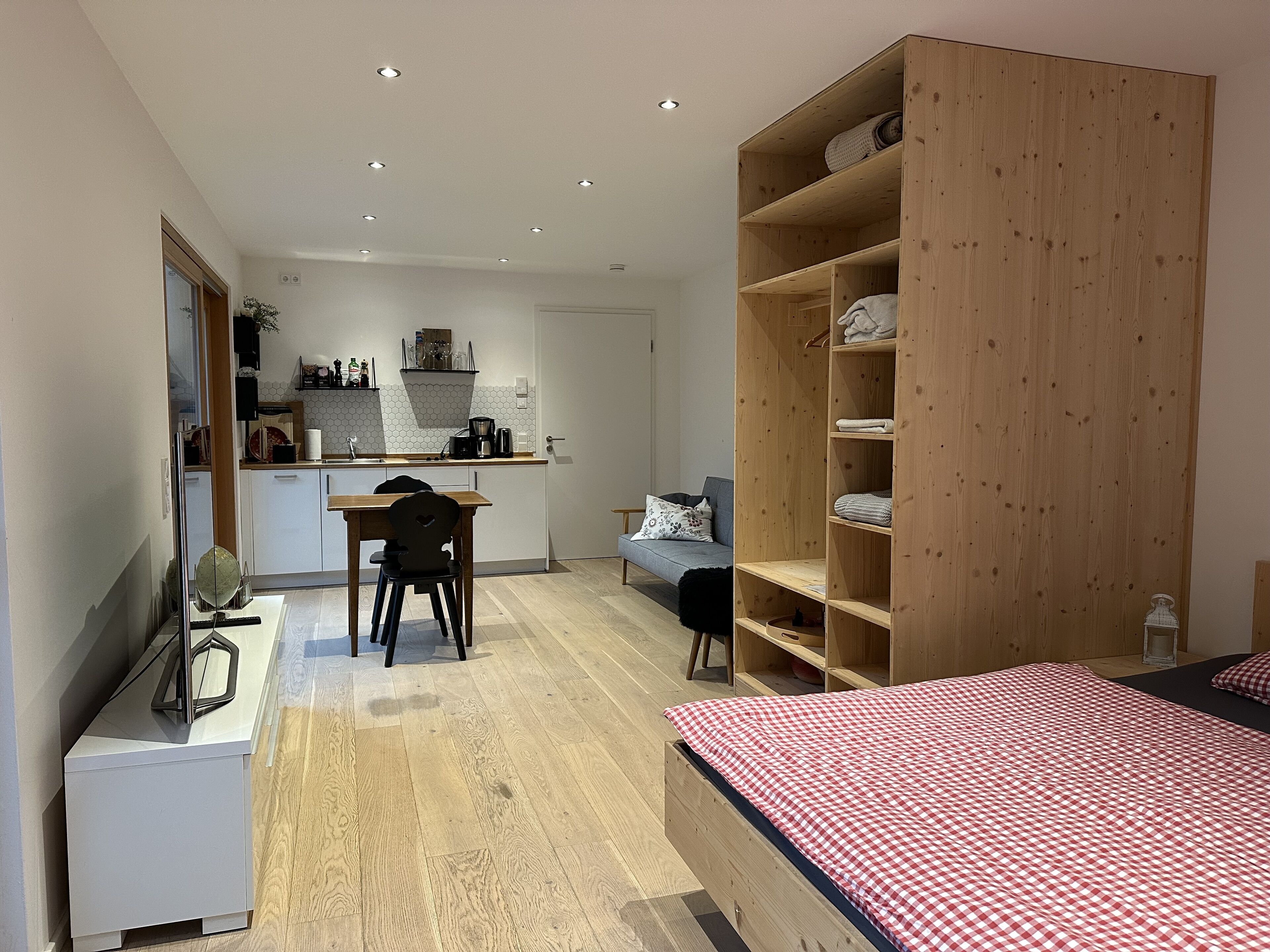 Ein modernes Schlafzimmer mit einem Holzbett, einem Schreibtisch mit Stuhl, einer Couch und einem Einbauschrank.